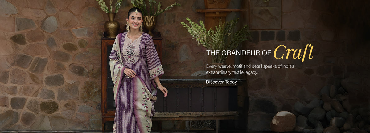 A woman models a traditional Indian salwar kameez suit in a rustic stone-walled room. The outfit consists of a lavender-purple and white patterned kurta with a matching purple kameez jacket, featuring intricate gold embroidery on the chest and sleeves. Bestseller purple handcrafted block print kurta suit set for women with matching dupatta - Mahee Jaipur bestseller collection